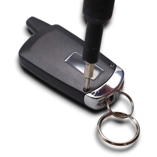 Close-up of a screwdriver tightening a screw on a black car key fob with a metal keyring attached.
