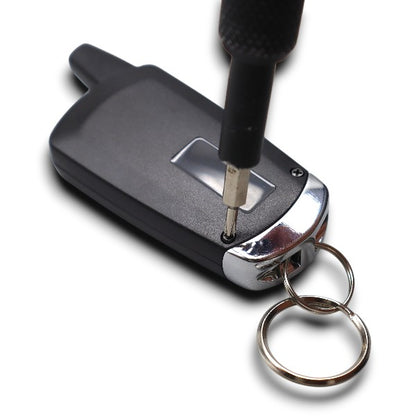 Close-up of a screwdriver tightening a screw on a black car key fob with a metal keyring attached.