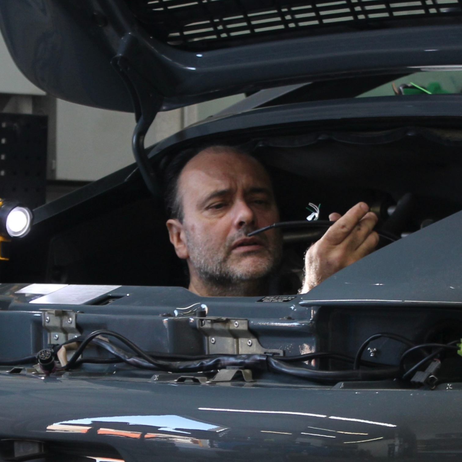 Technician performing professional car installation, working carefully under an opened vehicle hood with wiring visible