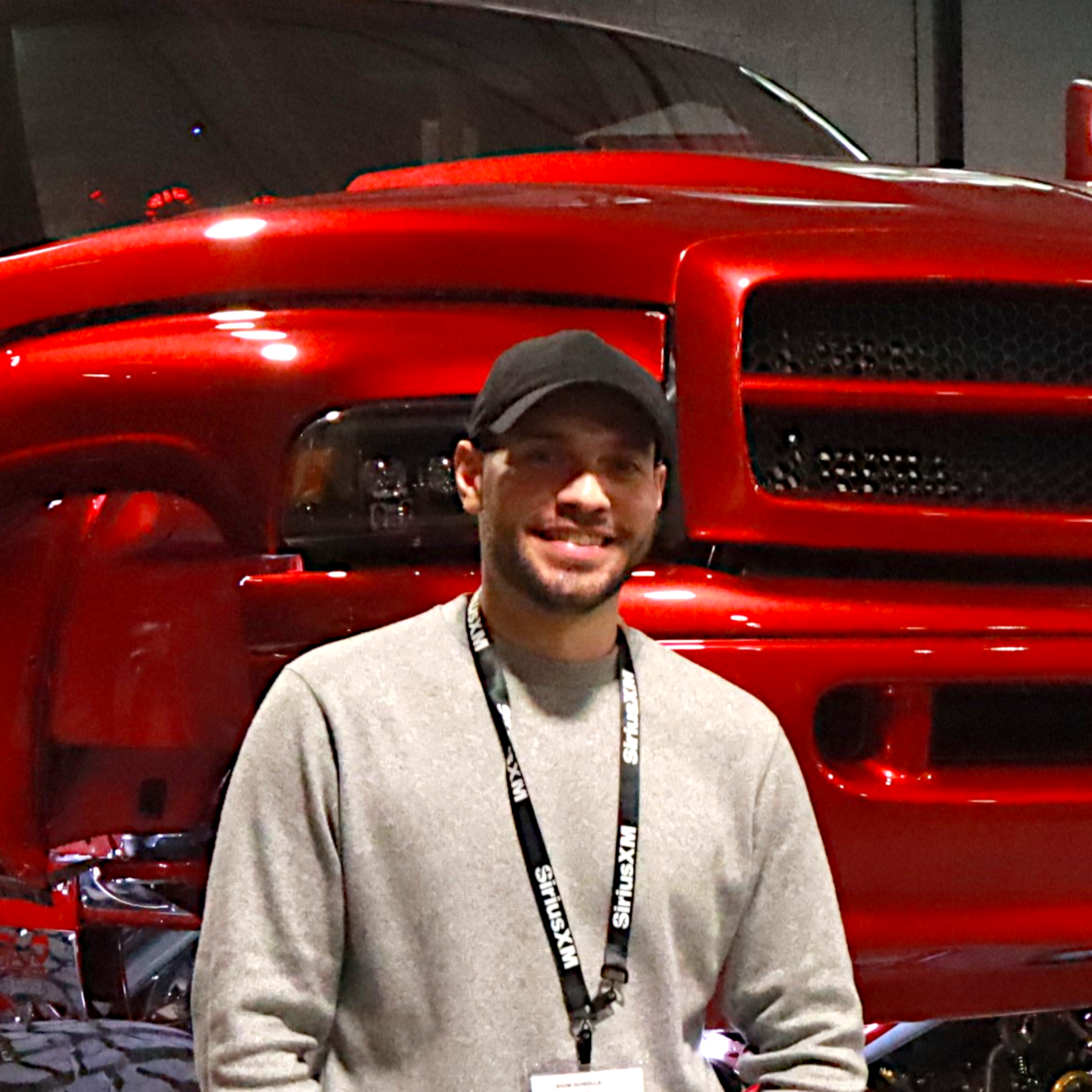 Man wearing cap and badge standing in front of a shiny red lifted truck in an indoor setting