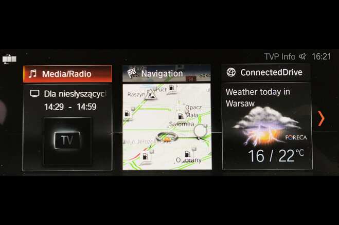 Car infotainment screen showing media playback, navigation map, and weather forecast for Warsaw at 16:21.