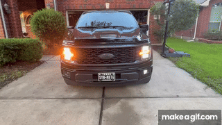 Black pickup truck parked in a residential driveway with one front turn signal illuminated during daytime